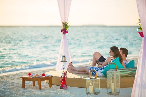 Paar am Strand vor dem Sun Siyam Iru Fushi Hotel, beide mit Weinglas, Blick auf das Meer