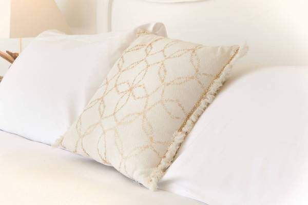 Ein weißes Kissen mit goldenen Mustern auf einem weißen Bett