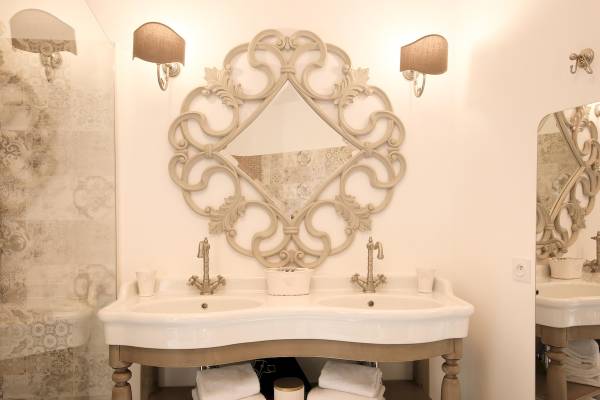 Badezimmer von L'Hostellerie du Moulin mit zwei Waschbecken und einer runden Wandspiegel.