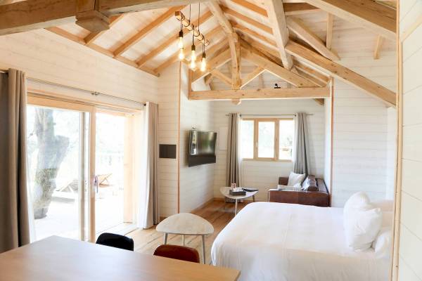 Innenansicht des Schlafzimmers im L'Hostellerie du Moulin Hotel mit weißem Bett, Couch, Fernseher und Glastür zum Balkon.