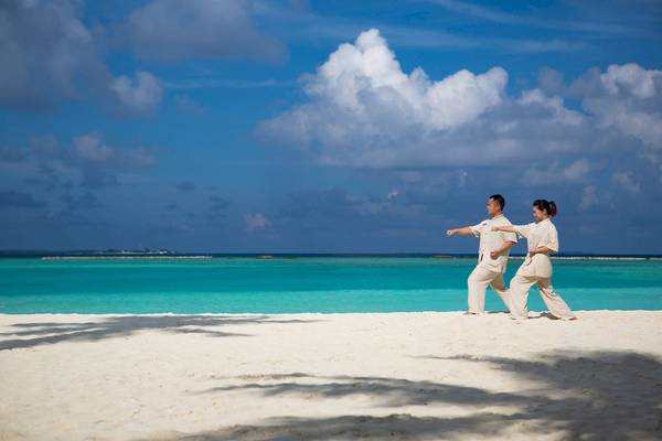 Zwei Personen praktizieren Yoga am Strand von Sun Siyam Iru Fushi.