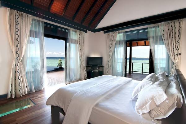 Schlafzimmer mit Meerblick im Sun Siyam Iru Fushi Hotel mit einem großen Bett, Fernseher und Glasboden.