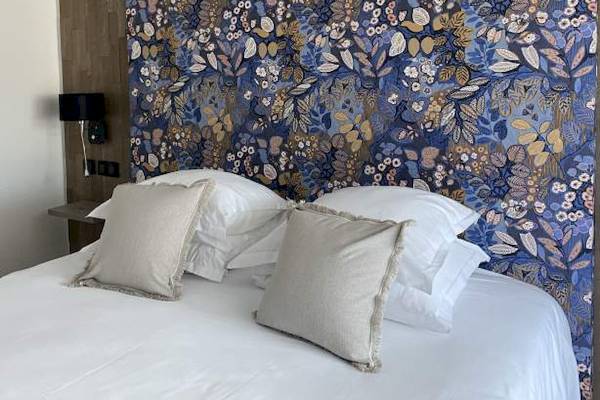 Ein Bett mit weißen Laken und Kissen vor einer blauen Blumentapete im Hotel La Lagune.