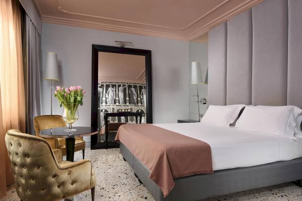 Foto eines luxuriösen Hotelzimmers mit Bett, Spiegel und Blumenvase von Leon's Place Hotel.