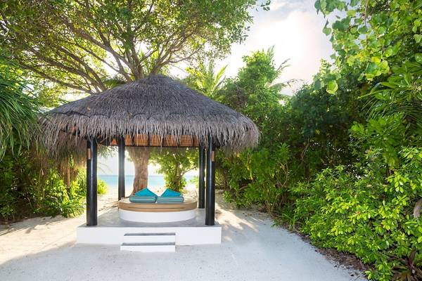 Gazebo am Strand im Sun Siyam Iru Fushi Hotel mit zwei blauen Kissen.