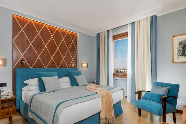 Schlafzimmer im Bettoja Hotel Mediterraneo mit blauem Kopfteil, Bettwäsche und Fenster mit Aussicht.