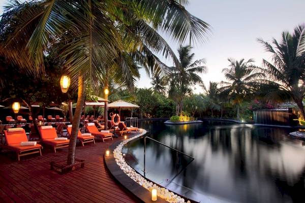 Pool-Lounge-Bereich im Sun Siyam Iru Fushi Hotel mit roten Liegestühlen und Palmen.