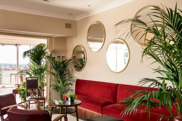 Innenbereich des Bettoja Hotel Mediterraneo mit roten Sofas, Pflanzen und runden Spiegeln.