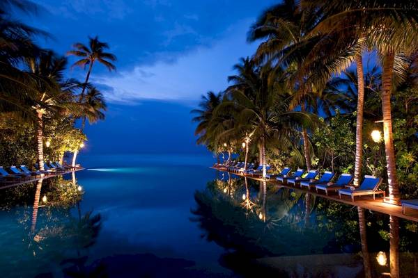 Nachtansicht des Infinity-Pools des Sun Siyam Iru Fushi Hotels mit blauen Liegen und Palmen