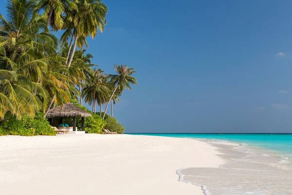 Sonnenuntergang am Strand von Sun Siyam Iru Fushi mit Blick auf einen kleinen Pavillon und Palmen.