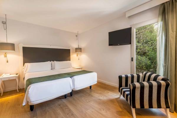 Innenansicht eines Doppelzimmers im ARTIEM Audax Hotel mit zwei Betten, Fernseher, Nachttischen und einem Sessel.