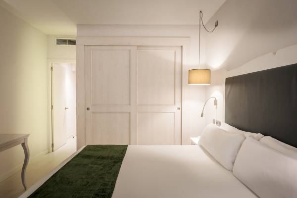 Schlafzimmer im ARTIEM Audax Hotel mit grüner Bettdecke und weißen Kissen.