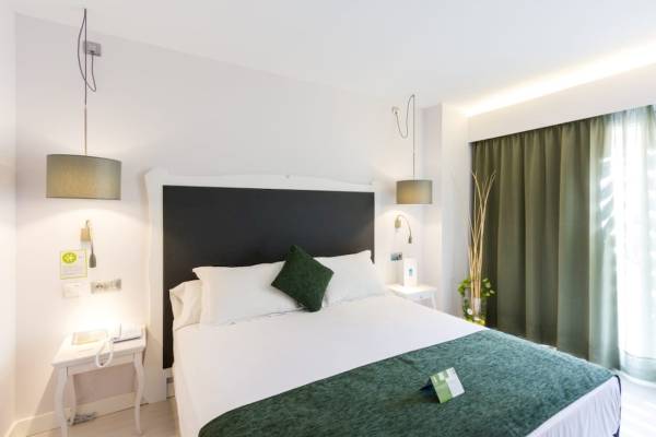 Hotelzimmer im ARTIEM Audax mit weißem Bett, grüner Decke und grünen Vorhängen.