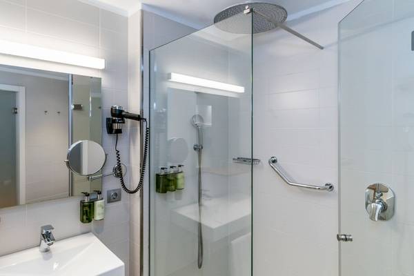 Badezimmer im ARTIEM Audax Hotel mit einer Glasdusche, Spiegel und Föhn.