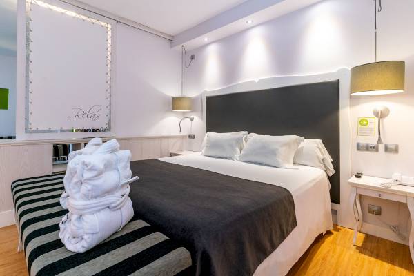 Ein stilvolles Hotelzimmer mit einem bequemen Bett, weißen Kissen und grauen Decken, umgeben von weißen Wänden und Holzboden.