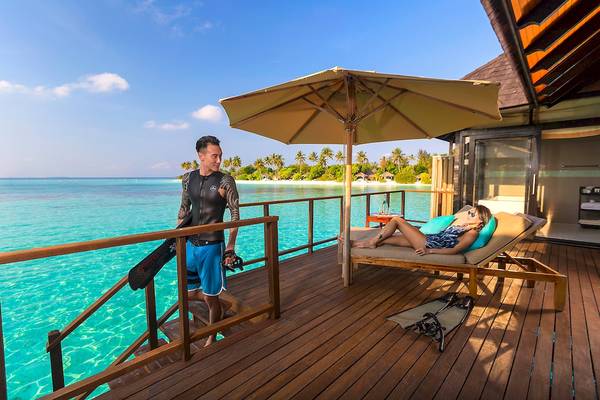 Mann und Frau auf der Terrasse des Sun Siyam Iru Fushi Hotels mit Blick auf das Meer.
