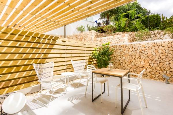 Sitzecke im Garten des ARTIEM Audax Hotels mit weißen Stühlen, Holztisch und Pergola