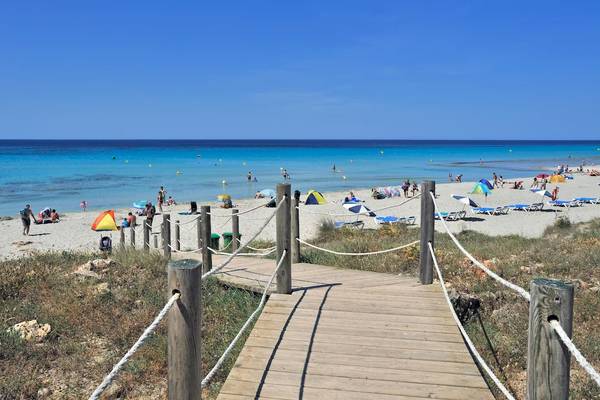 Ein sonniger Strand mit einem Holzsteg, vielen Sonnenschirmen und vielen Menschen, die sich entspannen.