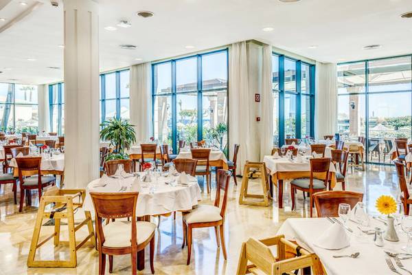 Innenansicht des Restaurants im Punta Prima Resort & Spa mit gedeckten Tischen und großen Fenstern.
