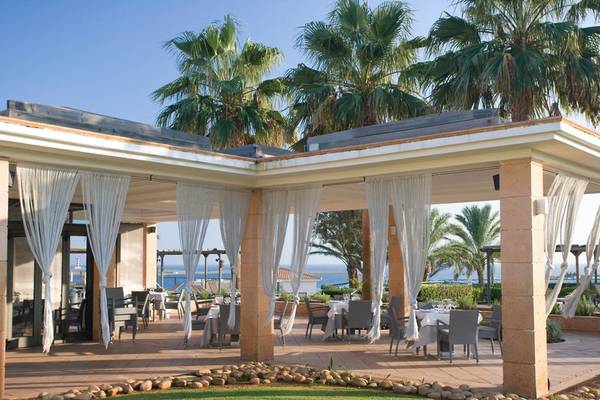 Terrasse des Punta Prima Resort & Spa mit Tischen, Stühlen und weißen Vorhängen.