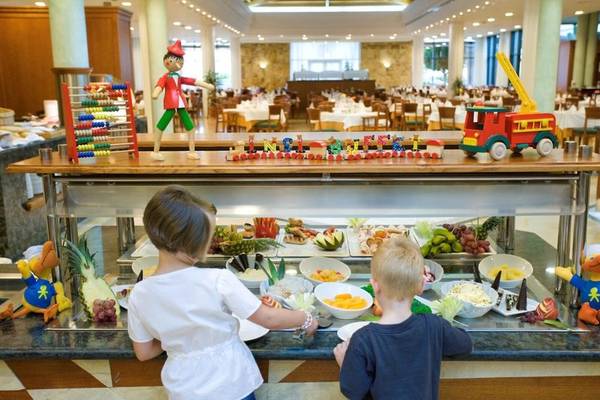 Zwei Kinder stehen vor einem Buffet im Punta Prima Resort & Spa mit verschiedenen Früchten und Dekorationen.