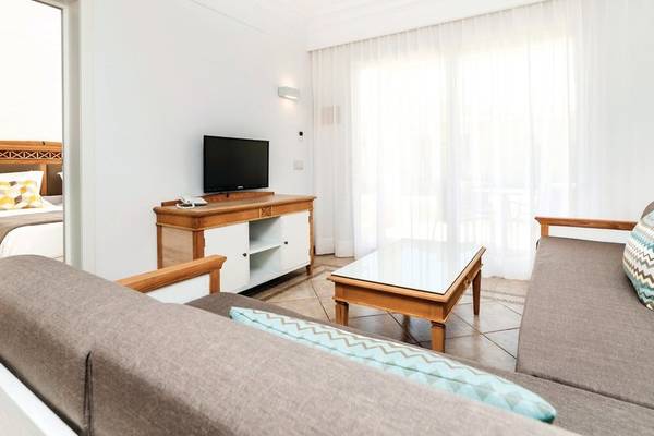 Wohnzimmer des Punta Prima Resort & Spa mit Fernseher, Sofa, Tisch und Bett im Hintergrund.