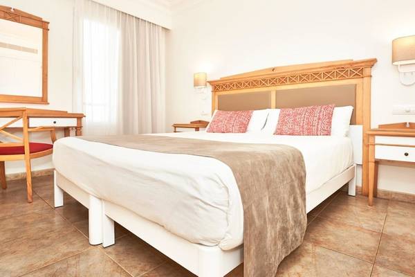 Schlafzimmer im Punta Prima Resort & Spa mit Doppelbett, Nachttischen und einem Fenster mit Vorhängen.