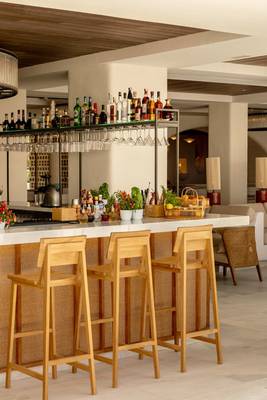 Innenansicht der Bar im Villa Le Blanc Gran Melia Hotel mit Holzstühlen und einer Theke voller Flaschen und Gläsern.