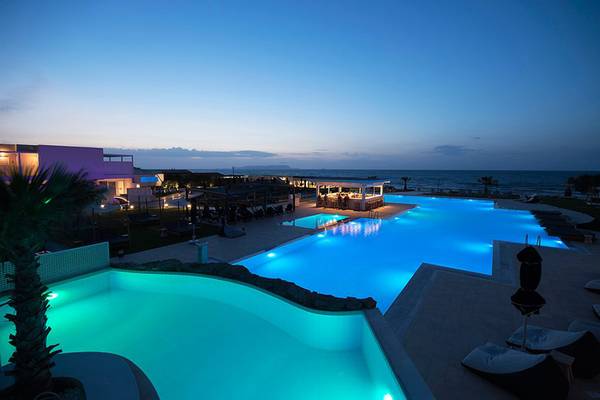 Der beleuchtete Pool des Insula Alba Resort & Spa bei Nacht am Meer.
