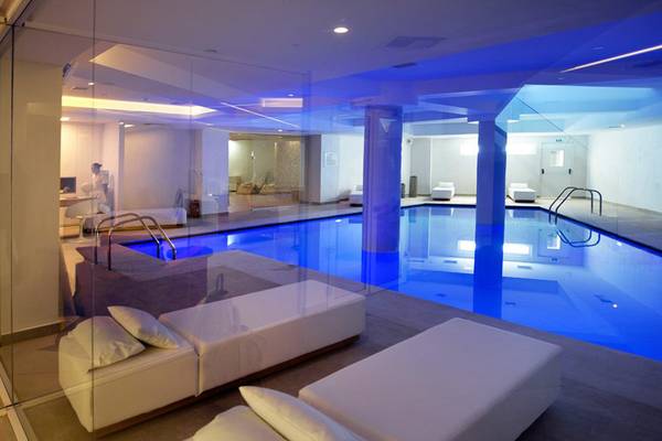 Pool-Bereich im Insula Alba Resort & Spa mit blauen Beleuchtung und weißen Liegestühlen.