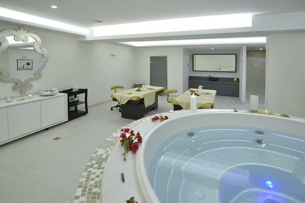 Behandlungsraum im Insula Alba Resort & Spa mit einem großen Whirlpool, zwei Behandlungstischen und einem Spiegel.