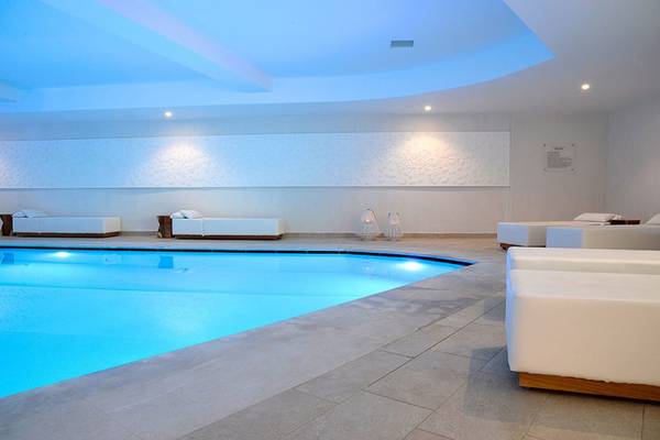 Innenpool des Insula Alba Resorts & Spa mit weißen Möbeln und blauen Lichtern.