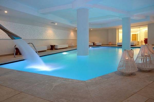 Innenpool im Insula Alba Resort & Spa mit Wasserfall und weißen Möbeln.