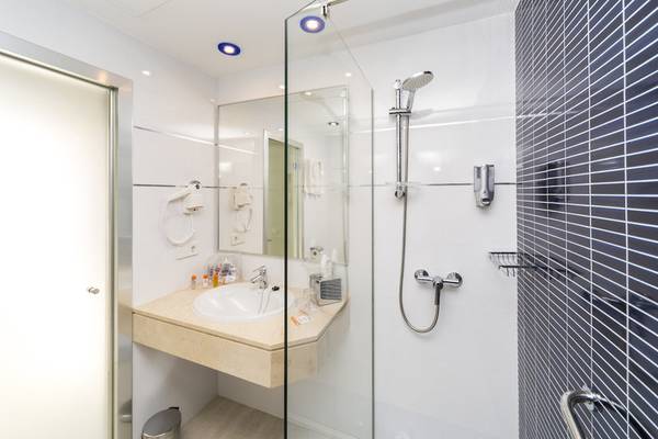 Badezimmer des Globales Lord Nelson Hotels mit Glasdusche, Waschbecken und Spiegel.