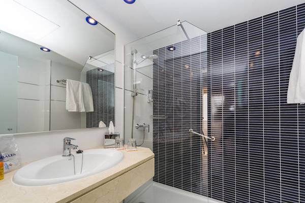 Ein Badezimmer im Hotel Globales Lord Nelson mit einer Dusche, einem Waschbecken und Spiegel.