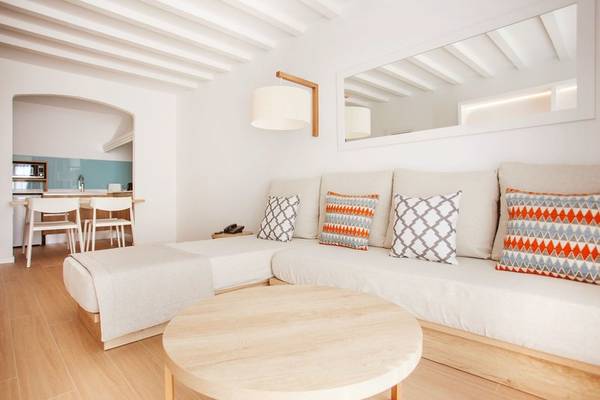 Wohnbereich des Grupotel Aldea Cala'n Bosch mit einem weißen Sofa, Kissen und Tisch.
