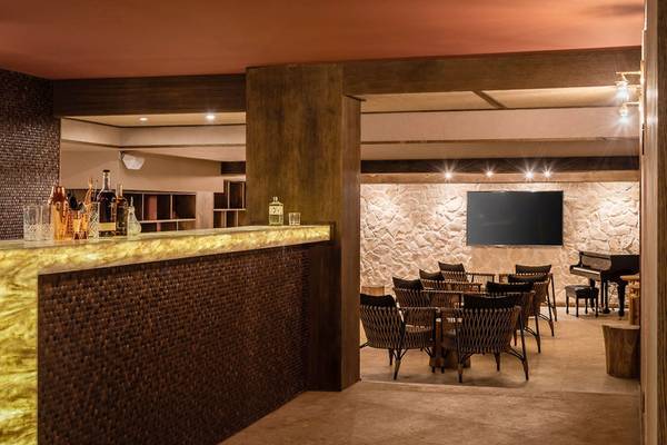 Die Bar des Lago Resort Menorca - Suites del Lago mit einer Theke, Möbeln und einer Fernsehwand.