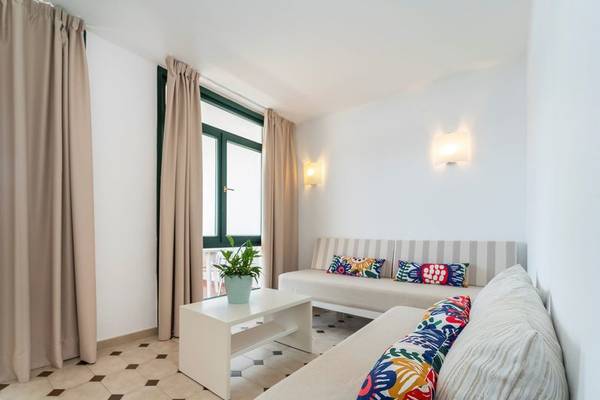 Innenraum eines Zimmers im Beach Club Menorca mit Sofa, Couch, Tisch, Fenster und Beleuchtung.