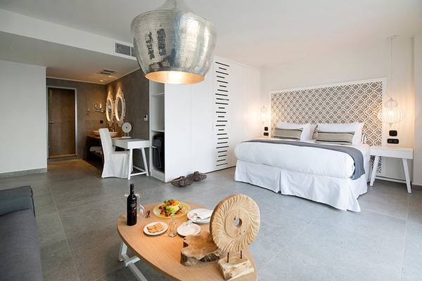 Schlafzimmer im Insula Alba Resort & Spa mit Bett, Nachttischen, Esstisch und Dekorelementen.