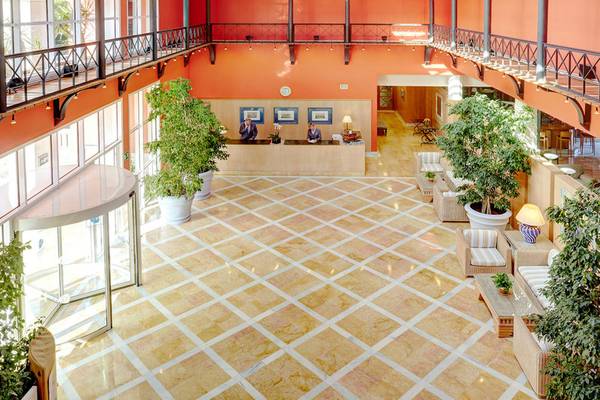 Empfangsbereich des Grupotel Playa Club Hotels mit orangefarbenen Wänden, geometrischem Bodenmuster und Pflanzen.