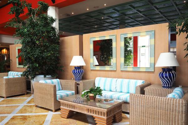 Lobby des Grupotel Playa Club mit Rattanstühlen, einem Glastisch und Spiegeln.