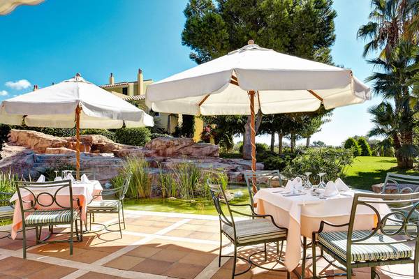 Außenterrasse des Grupotel Playa Club mit gedeckten Tischen unter Sonnenschirmen und Blick auf einen Wassergarten.