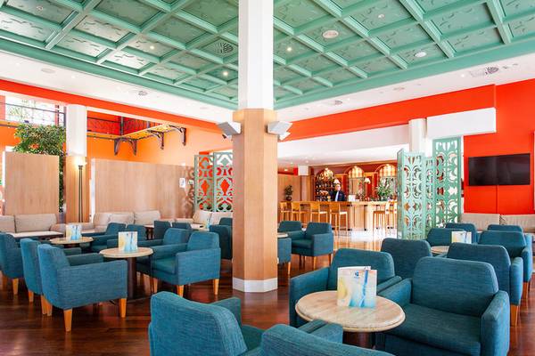 Loungebereich des Grupotel Playa Club mit blauen Stühlen, Holzboden und orangefarbenen Wänden.