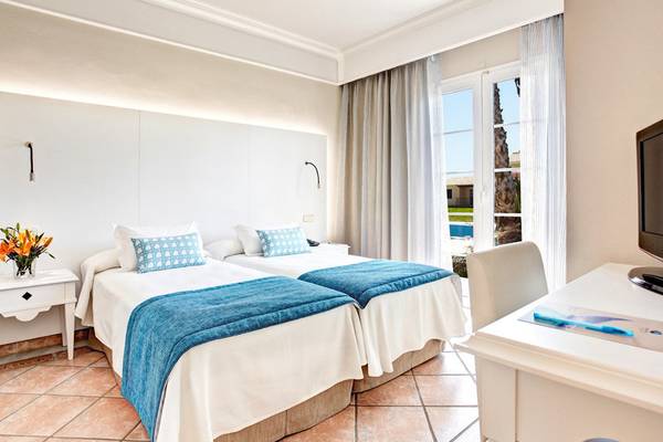 Doppelzimmer im Grupotel Playa Club mit zwei Betten, Tisch, Fernseher und einem Fenster mit Poolblick.