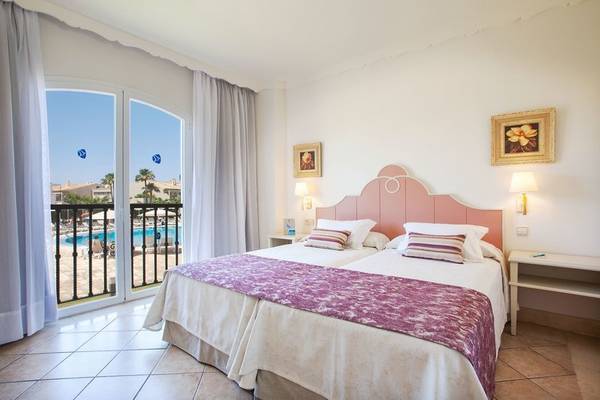 Schlafzimmer im Grupotel Macarella Suites mit Balkon und Blick auf den Pool.