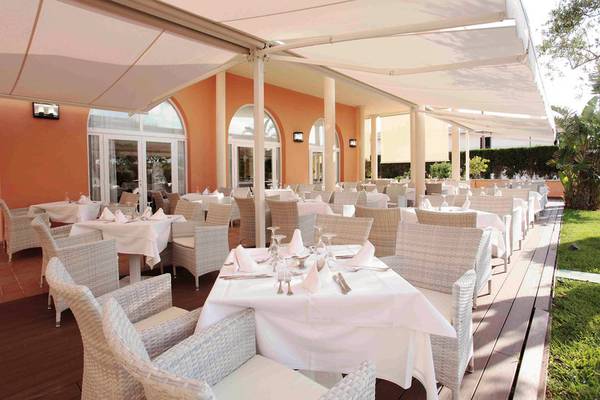 Terrassenrestaurant des Grupotel Macarella Suites & Spa mit weißen Tischen und Stühlen unter einem weißen Sonnensegel.