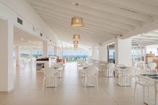 Innenansicht des Restaurants im Carema Beach Menorca Hotel mit weißen Möbeln und Blick auf das Meer.