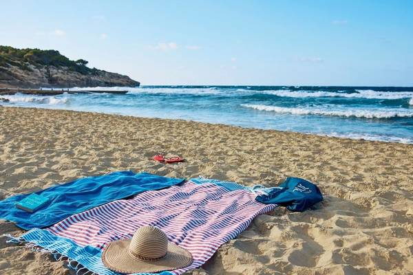 Ein Sonnenstrand mit blauen und roten Handtüchern, einem Buch und einem Hut.