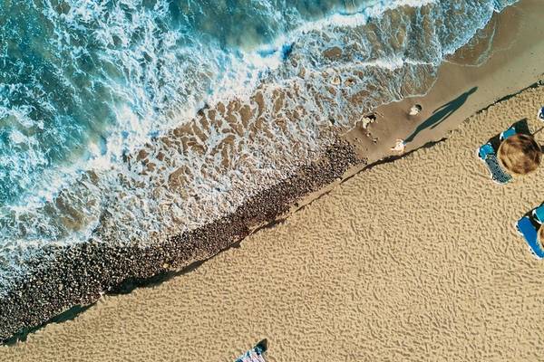 Oberflächenaufnahme von einem Strand mit Wellen und Sonne, mit Liegen und Handtüchern.