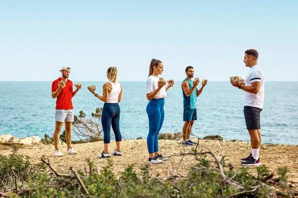 Gruppe von Menschen, die auf einem Strand Fitnessübungen mit Steinen machen, Victoria Menorca Hotel.